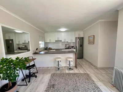 a kitchen with white cabinets and a table with stools at Private Garden Flat Blouberg Beach in Cape Town