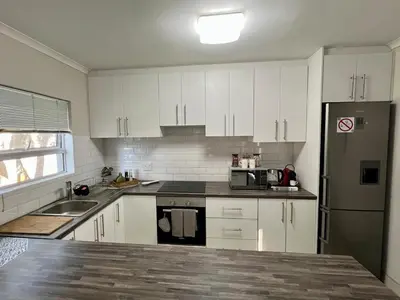a kitchen with white cabinets and a stainless steel refrigerator at Private Garden Flat Blouberg Beach in Cape Town