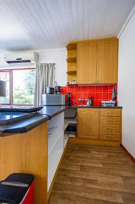 a kitchen with wooden cabinets and a red tile wall at Bed On Boucher in Durbanville