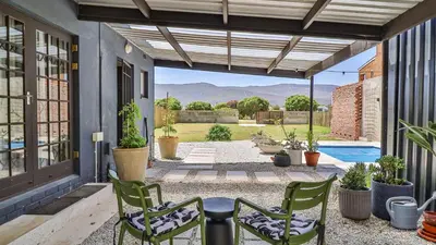 a patio with chairs and a table and a pool at Cozy Cottage in Hermanus