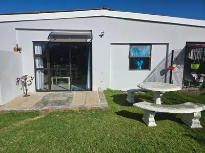 a white building with a bench in the grass at Cozy Cottage in Hermanus