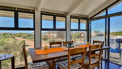 a dining room with a table and chairs and large windows at BluCabana 500m from Main Beach in Bettyʼs Bay
