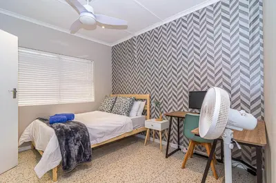 a bedroom with a bed and a desk with a fan at Pikkewyn Paradise in Hermanus