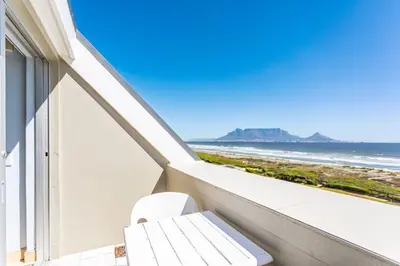 a white chair sitting on a balcony overlooking the beach at Dolphin Beach H305 in Cape Town