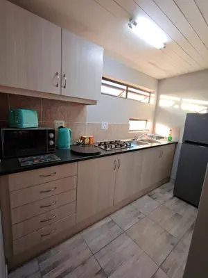 a kitchen with wooden cabinets and a black counter top at Sunbird Studio Apartment in Brackenfell