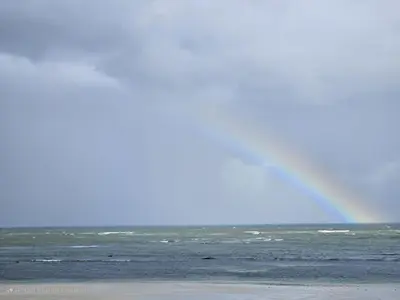 a rainbow in the sky over the ocean with a beach at Searenity Tides in Cape Town