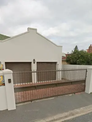 a white building with two garage doors and a fence at Pualani Self Catering in Strand