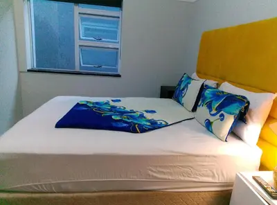 a bed with blue and white pillows and a window at Neo & Ruks Goodwood 1 in Goodwood