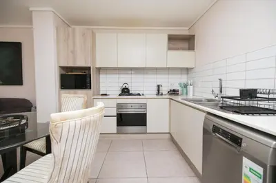 a kitchen with white cabinets and a table and chairs at 2 Bedroom Waters Edge Apartment in Century City in Cape Town