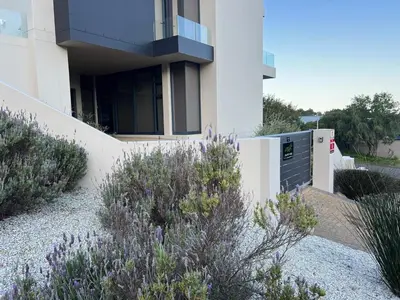 a white building with some purple plants in front of it at Suite Vos in Hermanus