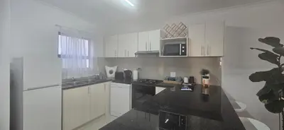 a kitchen with white cabinets and a black counter top at 118 on the Bay in Gordonʼs Bay