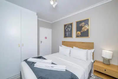 a bedroom with a white bed with a wooden headboard at Prime Executive Apartments 2 in Durbanville