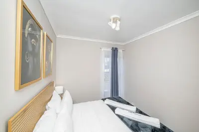 a white bedroom with a bed and a window at Prime Executive Apartments 2 in Durbanville