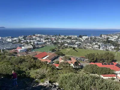 a man standing on top of a hill overlooking a town at Central Town Duplex with Pool, BBQ & Mountain View in Hermanus