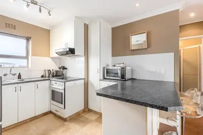 a kitchen with white cabinets and a black counter top at Modern City Apartment with Balcony & Braai in Cape Town