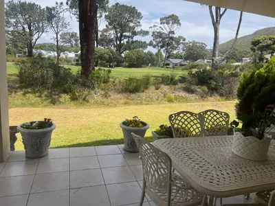 a table and chairs on a patio with a view of a field at Golfers paradise on 25th green in Hermanus
