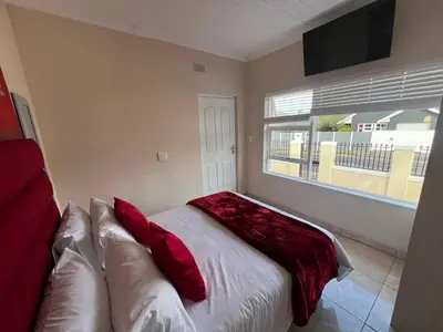 a bedroom with a bed with red pillows and a window at Minak Guest House Bellville in Bellville