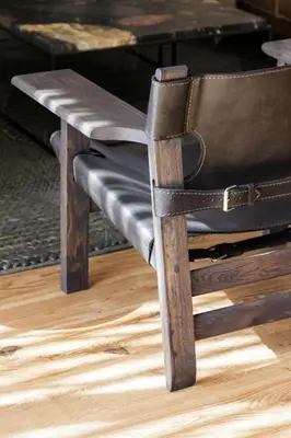 a wooden chair with a leather seat and a table at Tide and Timber Luxury Guesthouse in Hermanus