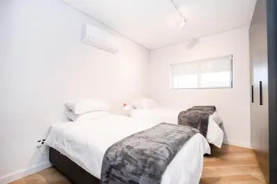 two beds in a bedroom with white walls and a window at Paarl - Lux Modern 2 Bedroom Apartment with Parking in Paarl