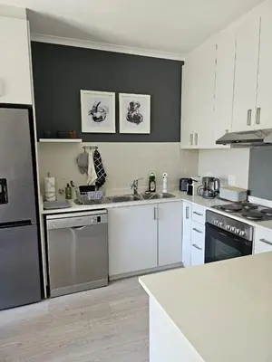 a kitchen with white cabinets and a black refrigerator at At Leisure Apartment 2 in Stellenbosch