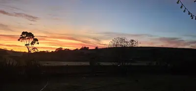 a sunset over a field with a fence and a hill at Hoopoe Cottage Horns op de Hoek in Hartebeest Rivier