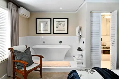 a white bathroom with a tub and a chair at Le Petit Bijou Aparthotel in Franschhoek