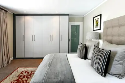 a bedroom with a large bed and white cabinets at Le Petit Bijou Aparthotel in Franschhoek