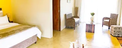 a bedroom with a bed and wicker chairs at Kapensis Guesthouse II Venue & self-catering in Bettyʼs Bay