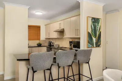 a kitchen with a counter with chairs around it at Elegant Apartment with Pool and Balcony Views in Cape Town