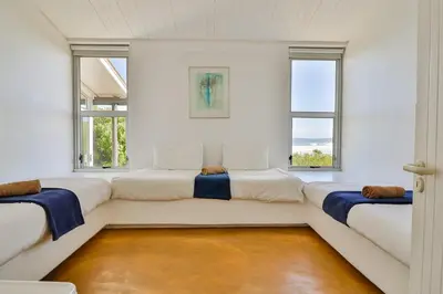 a white room with three beds and two windows at Turtle Drum ON THE BEACH in Bettyʼs Bay