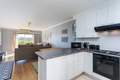 a kitchen with white cabinets and a living room at Century on Lake A45 by CTHA in Cape Town