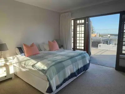 a bedroom with a large bed and a balcony at Voelklip Holiday Home in Hermanus