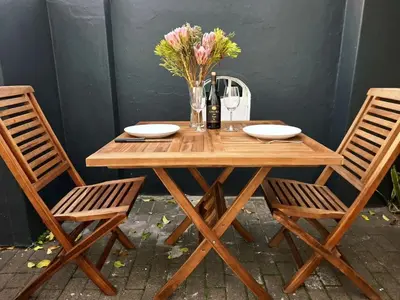 a wooden table with two chairs and a vase of flowers at The Harfield Hideaway in Cape Town