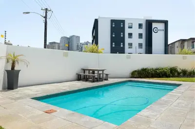 a swimming pool with a table next to a white wall at Beautiful Beach Break! in Cape Town