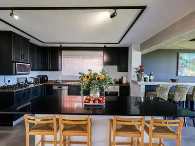 a kitchen with a black counter top and wooden chairs at Imoyo Ocean Retreat in Hermanus