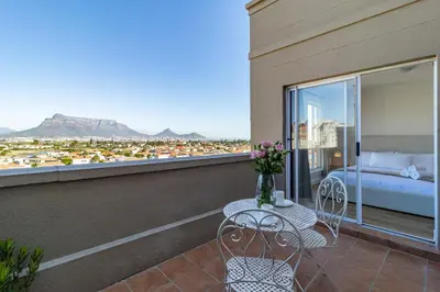 a balcony with a bed and a table with flowers on it at 2 Bedroom, Mountain View Penthouse, Century City in Cape Town