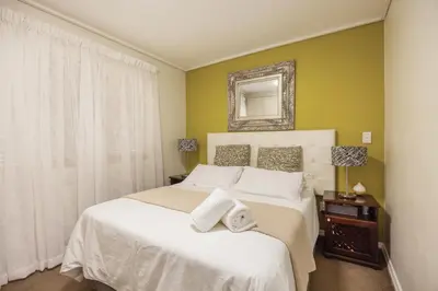 a bedroom with a white bed and a mirror at The Lagoon Beachfront Apartment in Cape Town