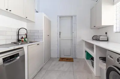 a white kitchen with white cabinets and a sink at Luxury Flamingo Villa at beach with Pool and Solar Back Up in Cape Town