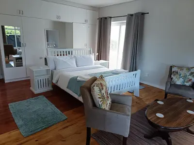 a bedroom with a bed and a chair and a table at Rockwest 1 Cosy summer holiday house Hermanus in Hermanus