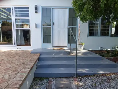 a white house with stairs leading to the front door at Rockwest 1 Cosy summer holiday house Hermanus in Hermanus