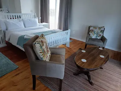 a bedroom with a bed and a chair and a table at Rockwest 1 Cosy summer holiday house Hermanus in Hermanus