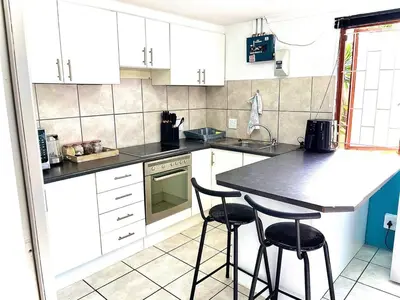 a kitchen with white cabinets and two bar stools at Cosy Flatlet in Chrismar in Stikland
