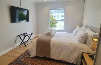 a white bedroom with a bed and a window at Breakwater Nr 4 holiday apartment in Hermanus