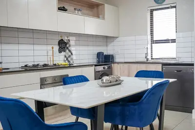 a kitchen with a white table and blue chairs at Walk to Canal Walk - Modern Flat in Cape Town