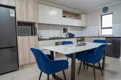 a kitchen with a white table and blue chairs at Walk to Canal Walk - Modern Flat in Cape Town