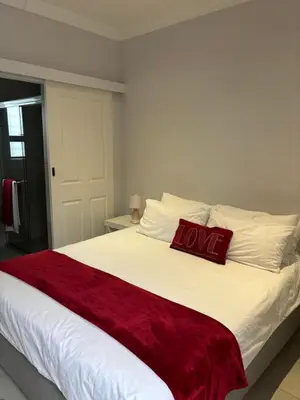 a large white bed with a red pillow on it at Studio Apartment in Cape Town in Cape Town
