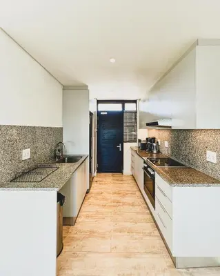 a kitchen with white cabinets and a wooden floor at Shiloh Apartment on Burmeister in Cape Town