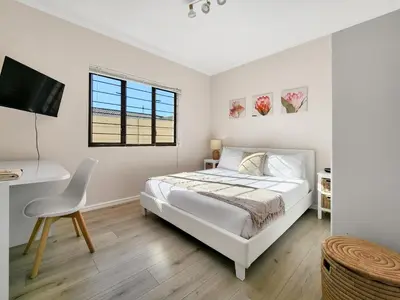 a white bedroom with a bed and a desk at Tranquil Garden Cottage in Cape Town