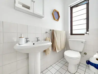 a white bathroom with a toilet and a sink at Tranquil Garden Cottage in Cape Town