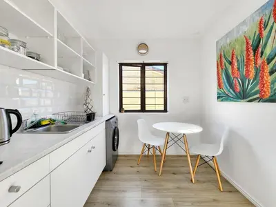 a white kitchen with a table and chairs in it at Tranquil Garden Cottage in Cape Town